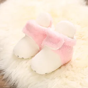 Primer plano de botas de nieve de felpa rosa y blanca para bebés en alfombra