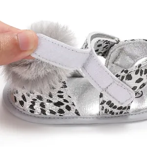 Close-up of hook-and-loop strap on silver leopard print baby sandals with pom-pom