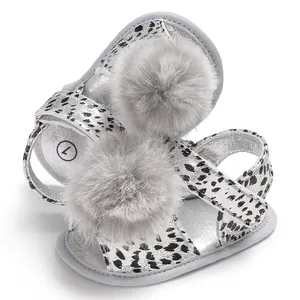 Close-up detail of silver baby sandals with leopard straps and grey fur pom-pom.