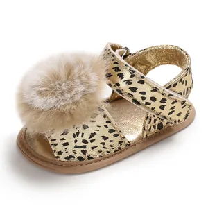 Detailed side view of a gold baby leopard print sandal with a large soft fur pom-pom