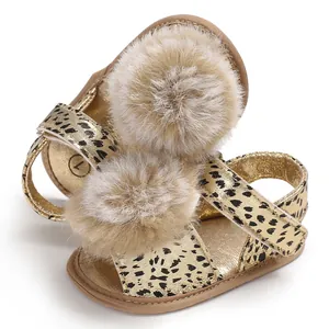 Close-up of gold leopard print baby sandals with soft faux fur pom-poms