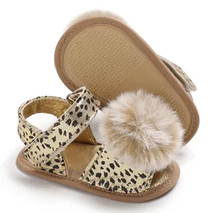 Close-up view of gold baby leopard print sandals with a large fluffy tan pom-pom detail
