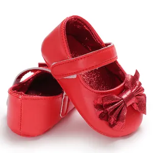 Vue détaillée de chaussures de princesse rouges pour bébé avec un grand nœud brillant.