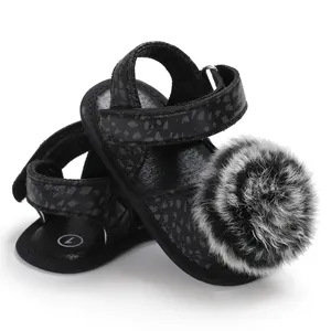 Close-up of black baby sandals with leopard texture and a fluffy grey pom-pom detail