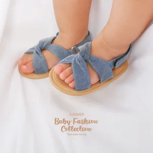 Primer plano de sandalias cruzadas de mezclilla azul para bebé sobre fondo blanco suave