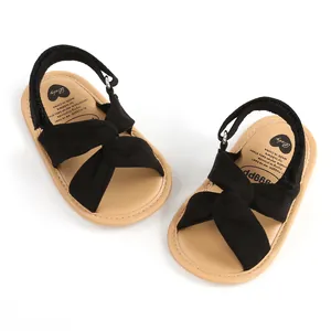 Detalle de sandalias negras para bebé con nudo cruzado y correas de velcro ajustable.