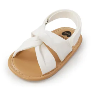 Detalle de sandalias blancas para bebé con tiras cruzadas y suela suave marrón