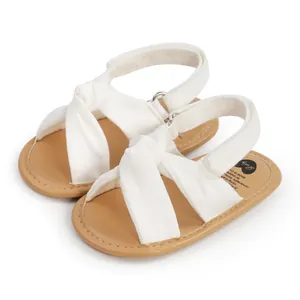Primer plano de sandalias blancas para bebé con tiras cruzadas y suelas tan