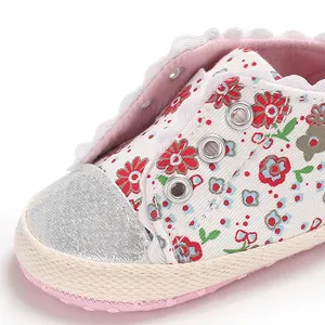 Macro detail of infant girls' floral print canvas shoes showing delicate lace and soft soles