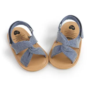 Detalle de sandalias de bebé en tela vaquera azul con diseño cruzado y suela marrón