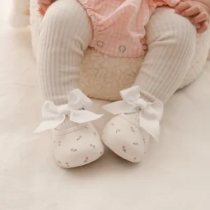 Nahaufnahme von Baby-Prinzessinnenschuhen mit Blumendruck und großer weißer Schleife