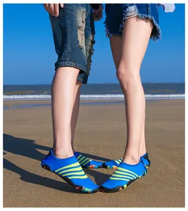 Paar dat blauwe en groene waterschoenen draagt op het zand met de zee op de achtergrond