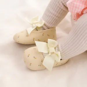 Nahaufnahme von geblümten Babyschuhen mit großen cremefarbenen Zierschleifen und weichen Sohlen
