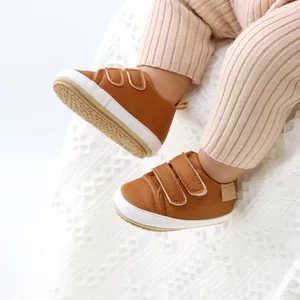 Close-up of baby feet wearing brown faux leather sneakers with double velcro straps