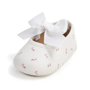 Nahaufnahme von weißen Baby-Prinzessin-Schuhen mit großer Schleife und rosa Blumenmuster