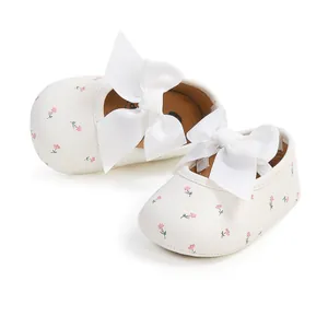 Nahaufnahme von weißen Baby-Prinzessinnenschuhen mit rosa Blumenmuster und großer weißer Schleife