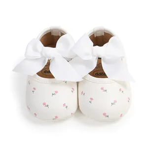 Nahaufnahme von weißen Babyschuhen mit rosa Blumenmuster und großen weißen Schleifen