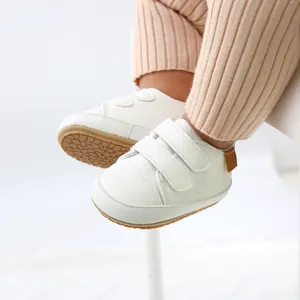 Close-up detail of white faux leather baby sneakers featuring double hook-and-loop straps.