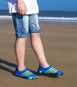Kind draagt blauwe en groene gestreepte waterschoenen op een zonnig strand