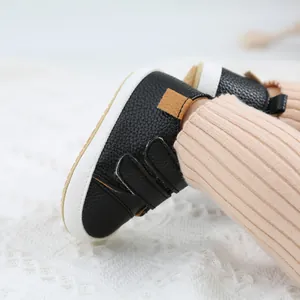 Close-up of black leather baby walking shoes with velcro straps on knitted background.