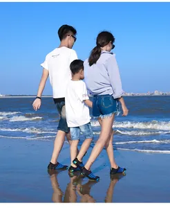 Een gezin van drie draagt gestreepte waterschoenen en wandelt op het zonnige strand