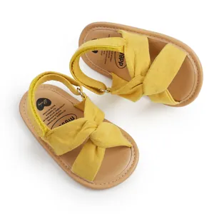 Sandalias de tela amarillas para bebé con diseño de tiras cruzadas y suelas marrones suaves