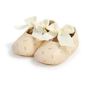 Detailansicht von cremefarbenen Baby-Lauflernschuhen mit Schleifen und Blumendruck