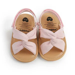 Primer plano de sandalias rosas para bebé con un diseño decorativo de nudo cruzado.