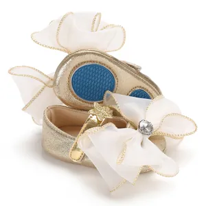Close-up of gold baby princess shoes with white organza bow and non-slip blue rubber sole.
