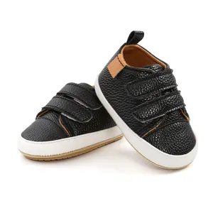Close-up of black pebbled leather baby pre-walker shoes with white soles and Velcro straps.