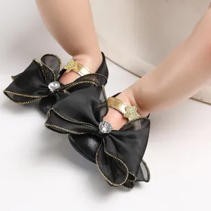 Detailed view of black baby girl princess shoes featuring large bows and gold trim.
