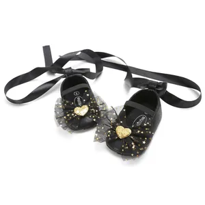 Detailaufnahme schwarze Baby-Prinzessinenschuhe mit goldener Herz- und Sternenschleife.