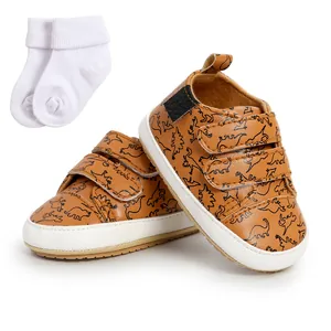Detail of infant walking shoes featuring a brown dinosaur pattern and Velcro straps.