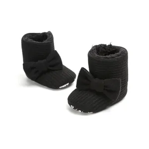 Close-up of black plush-lined baby snow boots with elegant bow details and soft soles.