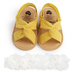 Sandalias amarillas para bebé con tiras cruzadas y diadema de flores blancas para niños.