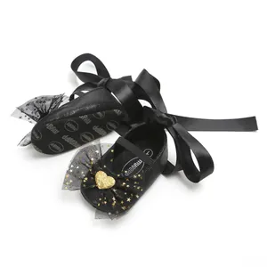 Detailaufnahme von schwarzen Baby-Prinzessin-Schuhen mit Satinbändern und Goldherz-Schleife