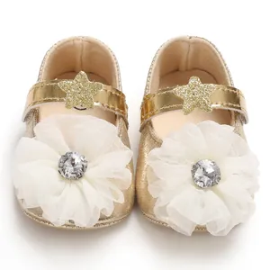 Close-up of gold baby girl princess shoes featuring large white fabric flowers and crystals