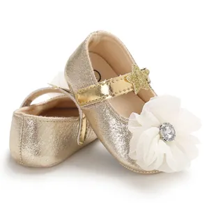 Close-up of sparkling gold baby princess walking shoes with a white chiffon flower