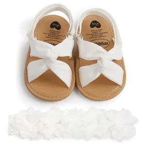 Detalle de las sandalias blancas para bebé con tiras cruzadas y diadema de flores.