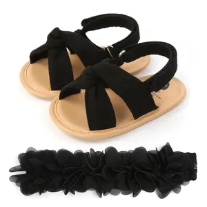 Detalle de sandalias negras para bebé con nudo cruzado y diadema de flores a juego