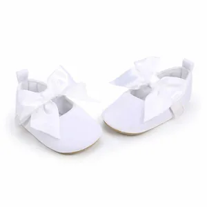 Detail van witte babyschoentjes voor de eerste stapjes met grote satijnen strikken