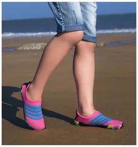 Kind met levendige roze en blauw gestreepte waterschoenen op een zonnig zandstrand.