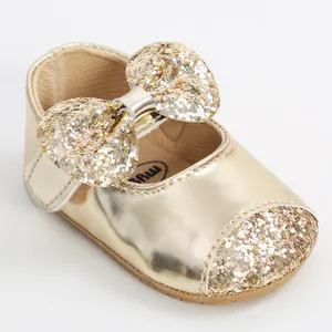 Close-up detail of a shiny gold baby girl princess shoe with a sparkling glitter bow.