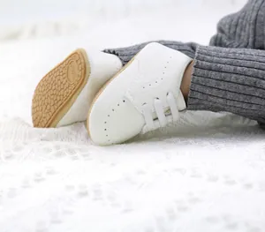 Close-up detail of white soft-soled PU leather baby shoes on a white knitted blanket