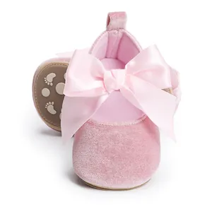 Close-up van roze fluwelen babyschoentjes met een grote satijnen strik en antislipzool