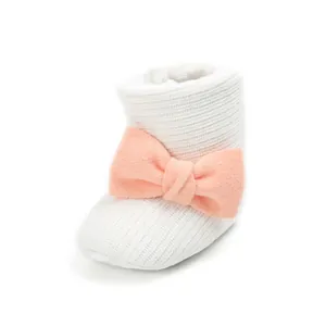 Detailed view of white knitted baby snow bootie with soft pink bow decoration