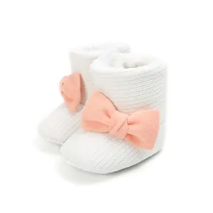 Side view of white knitted baby winter boots with plush lining and a large pink bow.