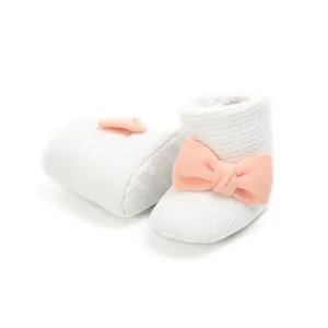 Close-up view of white knitted baby booties featuring a pink bow and warm fleece lining