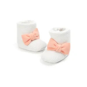 Close-up of white knitted baby boots with a soft plush lining and pink bow detail.