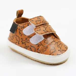 Close-up of brown baby walking shoes featuring black dinosaur prints and velcro closures